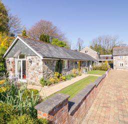 Stone houses with slate roofs and garden area along paved driveway at FernGully in St Columb Major