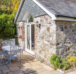 A stone building with slate roof and glass door next to a patio table and chairs at FernGully in St Columb Major