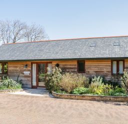 A wooden house with a gray slate roof and planted shrub beds at Kingcup Cottage in St Columb Major