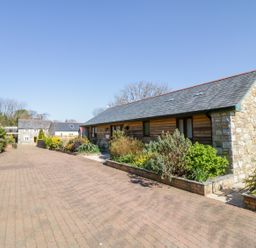 An outdoor paved driveway with stone and wooden buildings and garden beds at Kingcup Cottage in St Columb Major