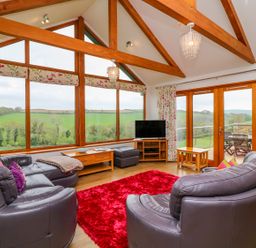 A living room with leather sofas a red rug large windows and wooden beams at Kingcup Cottage in St Columb Major