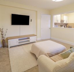 A living room with a wall mounted tv a cabinet a white door and a window to the kitchen at Beside The Sea - In Town in Llandudno