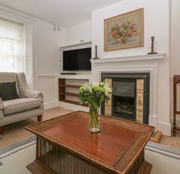 A living room with an armchair a wooden coffee table with a flower vase a fireplace and a TV at Dolphin House in Burford