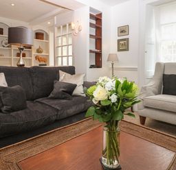 A living room with a dark sofa and light armchair and flowers on a wooden coffee table at Dolphin House in Burford
