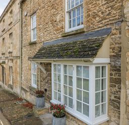 Stone exterior of a building with white framed windows and planting pots on a narrow street at Dolphin House in Burford