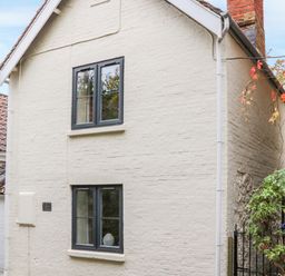 An exterior view of a two-story white brick house with black framed windows and a tiled roof at Tillys Cottage in Edington