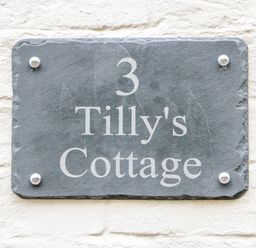 A stone house number plaque with the text 3 Tilly's Cottage on a white brick wall at Tilly's Cottage in Edington