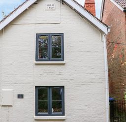 The exterior of a two-story building with white painted brick walls and two windows at Tilly's Cottage in Edington