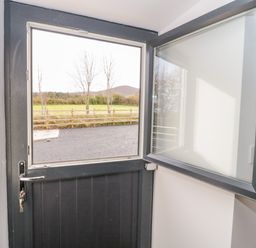 An open stable door with a window showing a fenced grassy field and trees at Rhydau Cottage in Pentir near Deiniolen