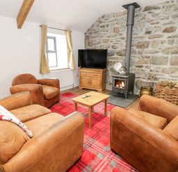 A living room with brown armchairs a wood burning stove a television and a red plaid carpet at Rhydau Cottage in Pentir near Deiniolen
