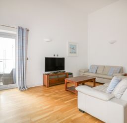 A living room with two sofas a wooden coffee table a TV on a wooden stand and glass doors with curtains at 28 Zenith in Porth