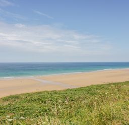 A sandy beach with scattered people and ocean waves viewed from a grassy hill at 28 Zenith in Porth