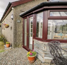 Exterior view of a stone and pebble covered house entrance with a potted plant and metal outdoor furniture at Melin Newydd in Porthmadog