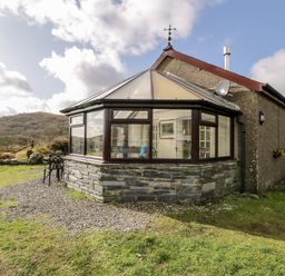 Exterior view of a house with a conservatory and a small table with two chairs outside on a gravel area at Melin Newydd in Porthmadog