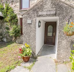 Stone house entrance with a wooden door a flower pot on the ground and a hanging flower basket at Bwthyn Pennant in Porthmadog