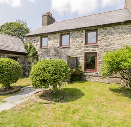 A stone cottage with three windows and two shrubs in the garden at Bwthyn Pennant in Porthmadog