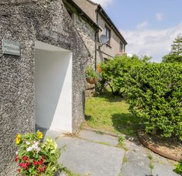 Exterior entrance to a stone house with a garden path and green bushes at Bwthyn Pennant in Porthmadog