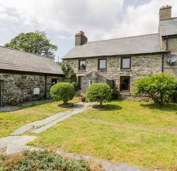 A stone house with a slate roof and a garden with shrubs and a stone path at Bwthyn Pennant in Porthmadog