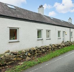 A house with windows and a door next to a stone wall at Ael Y Bryn Menai Bridge