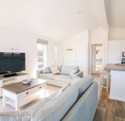 A living room with sofas TV and coffee table next to a kitchen island with stools at Ash Lodge in Teigngrace near Newton Abbot
