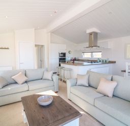A living room with two sofas and a wooden coffee table open to a kitchen with stools and dining table at Ash Lodge in Teigngrace near Newton Abbot