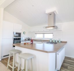A kitchen with a wooden countertop island with two stools and built in appliances at Beech Lodge in Teigngrace near Newton Abbot