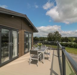 A deck with a table and four chairs outside a wooden house with glass doors at Beech Lodge in Teigngrace near Newton Abbot