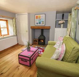 A living room with a green sofa pink trunk coffee table a fireplace and a window at Cottage on the Common in Westbury-on-Severn