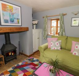 A living room with a green sofa and floral cushions a black wood stove and a colorful rug at Cottage on the Common in Westbury-on-Severn