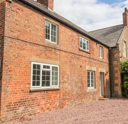 An exterior view of a brick house with multiple windows a door and a gravel ground at Well House Farm Flat 1 in Bretton