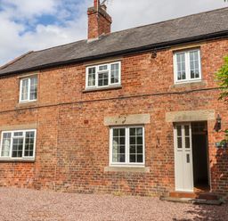 A two-story brick house with white windows and an open white door at Well House Farm Flat 1 in Bretton