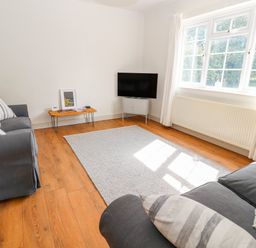 A living room with two gray sofas a small wooden table a television on a stand and a large window at Well House Farm Flat 1 in Bretton