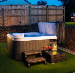 An outdoor hot tub on artificial grass with steps towels drinks and a lantern at Be Our Guest Cottage in Chacewater near Truro