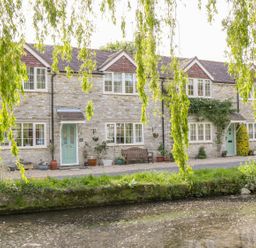 Stone cottages with pale green doors and windows by a small waterway with overhanging tree branches at Duck Cottage in Sutton Poyntz