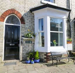 The front entrance of a brick house with a black door and a bay window with flowers in pots and a bench outside at Sailors Lodge in Filey