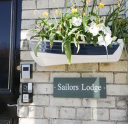 A wall with a planter of flowers above a sign reading Sailors Lodge beside a black door at Sailors Lodge in Filey
