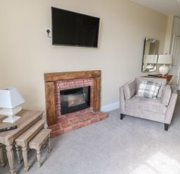 A living room with a grey armchair a brick fireplace and nested wooden side tables at Coquet View Apartment in Warkworth