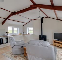 An open plan living area with kitchen cabinets a stove two leather chairs a wood burning stove and a TV on a wooden stand at Village View in Burton Bradstock