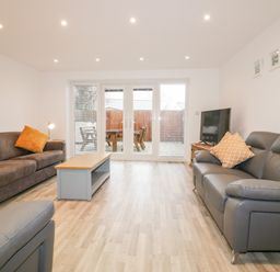 A living room with two sofas a coffee table a television and glass doors looking out to a patio at Lily Cottage in Camelford