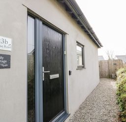 A black front door with address signs on a building with a gravel path alongside at Lily Cottage in Camelford