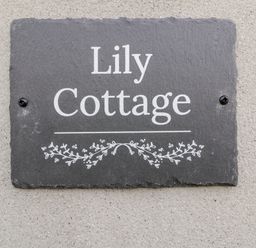A slate house name plaque with Lily Cottage and decorative vine design