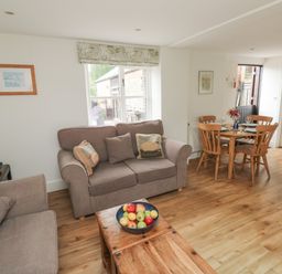 A living room with two sofas a wooden coffee table with a bowl of fruit and a dining table with four chairs at Bantam Cottage in Little Woodford near Ottery St Mary