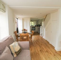 A living room with a sofa pillow dining table and chairs kitchen and TV on a wooden table at Bantam Cottage in Little Woodford near Ottery St Mary