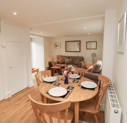 A dining area with a wooden table set for four and a living room with sofas and a coffee table at Bantam Cottage in Little Woodford near Ottery St Mary