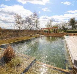 An outdoor natural swimming pool with plants in water and wooden deck at Tickmorend Farm in Nailsworth