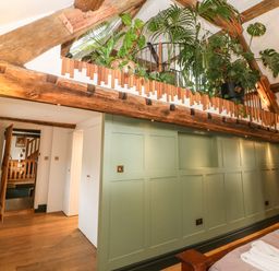 An interior room with green paneled wall wooden ceiling beams plants on loft and wooden furniture at Tickmorend Farm in Nailsworth