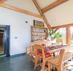 A dining room with wooden benches and chairs around a table with a patterned runner and a wooden bookshelf against the wall at Tickmorend Farm in Nailsworth