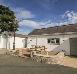 An outdoor patio with a picnic table stone walls and a green door at Buarthau Cottage in Llanrug