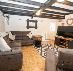 A living room with brown sofas a patterned rug a television on a wooden stand and exposed ceiling beams at Buarthau Cottage in Llanrug