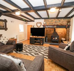 A living room with brown sofas a wood stove and a television at Buarthau Cottage in Llanrug